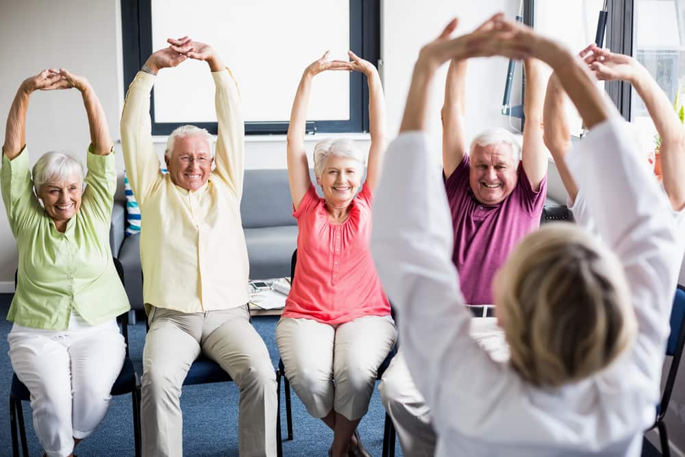 A group of elderly people enjoying an exercise class seated.