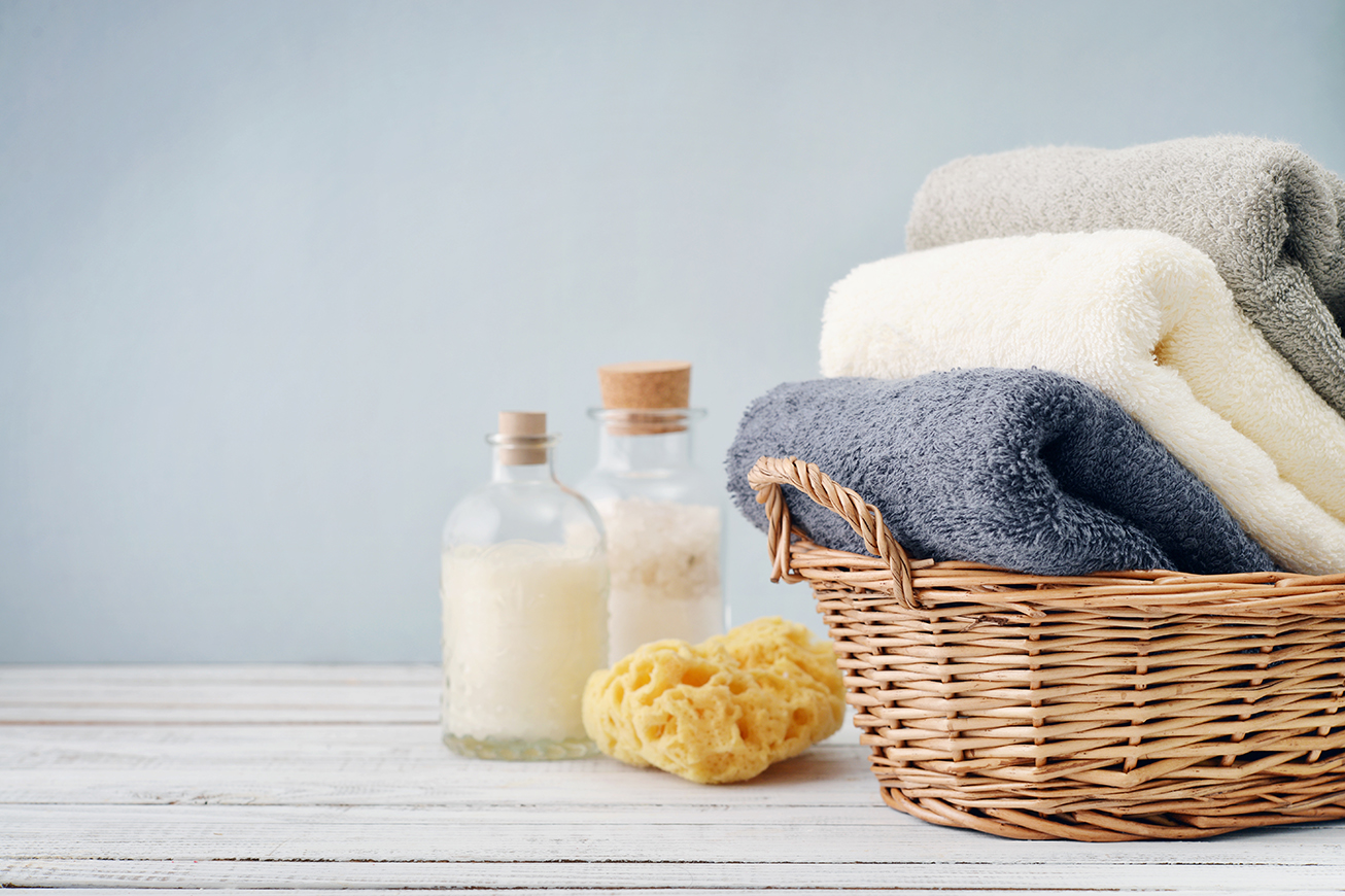 Bath towels of different colors in wicker basket on light background