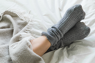 Feet in grey socks on a bed with a cosy blanket.