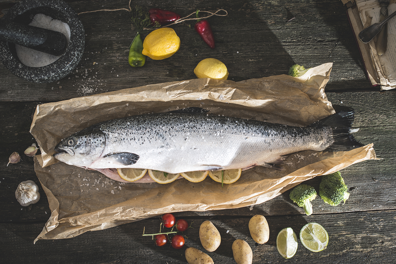 Preparing whole salmon fish for cooking. Vegetables on the table. Vintage style